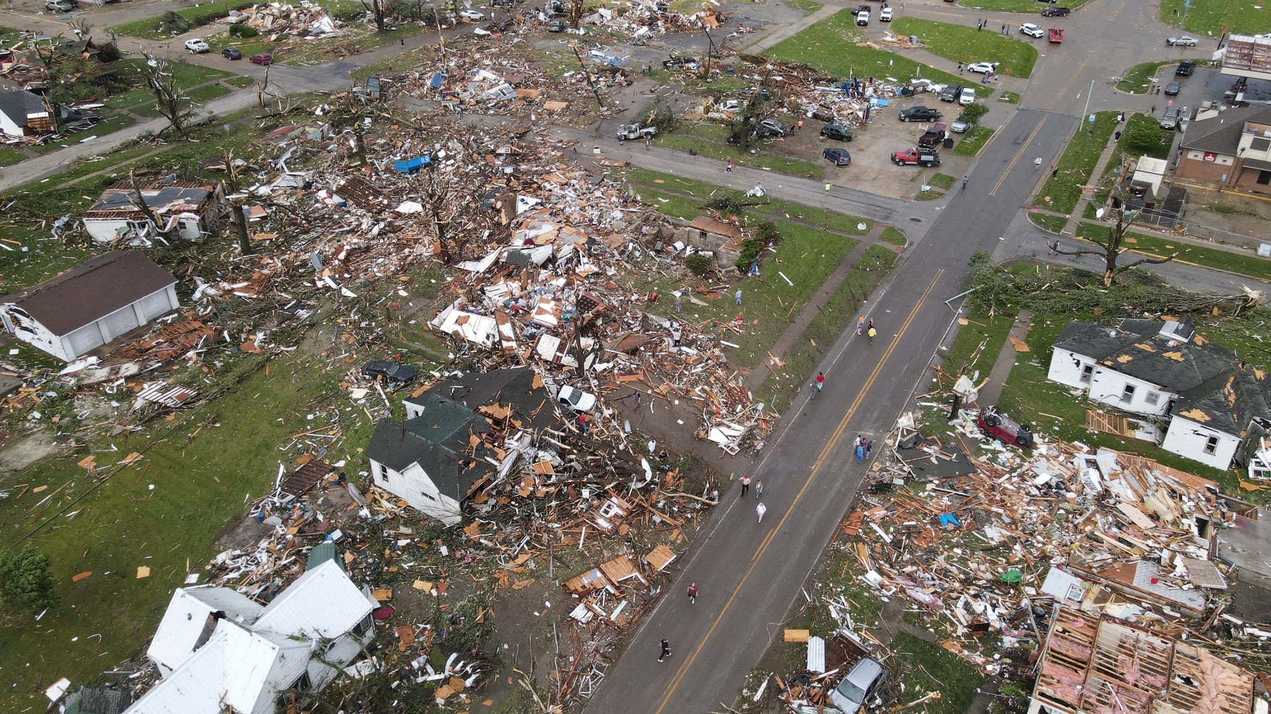 Aerial drone storm damage photo showing debris, damaged homes, streets, and emergency response activity