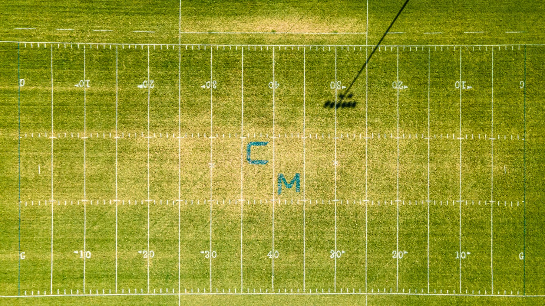 Aerial drone photo looking straight down at a football field with yard markings and a drone shadow